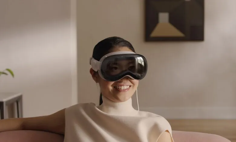 Woman smiles wearing Apple Vision Pro headset in a bright, modern living room.