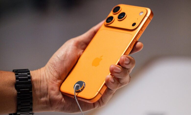Hand holding an orange iPhone with a security tether attached.