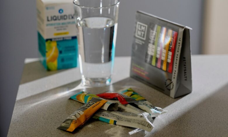 Liquid I.V. and LMNT electrolyte packets with a glass of water.