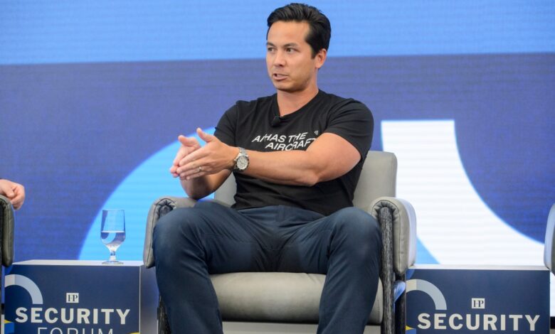 Man in black shirt gestures while seated at Security Forum.