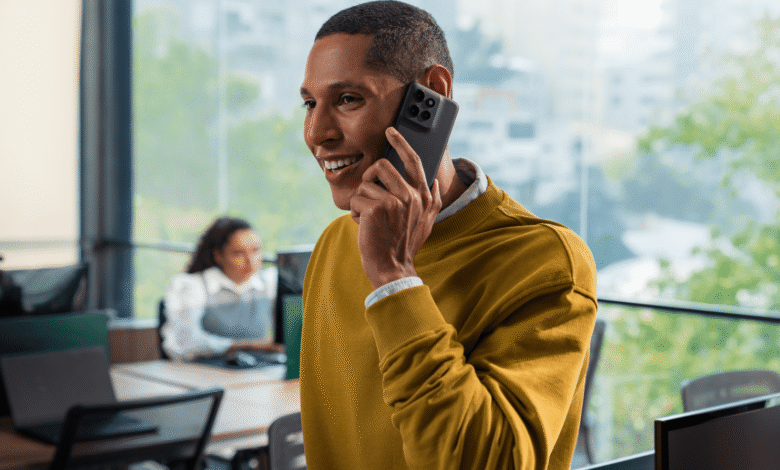Smiling man in yellow sweater talks on smartphone in modern office.