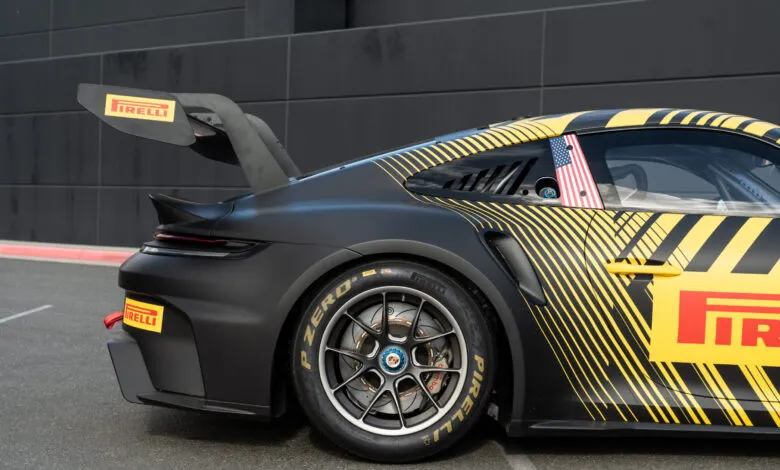Close-up of a matte black Porsche 911 Cup race car with yellow stripes and Pirelli branding.
