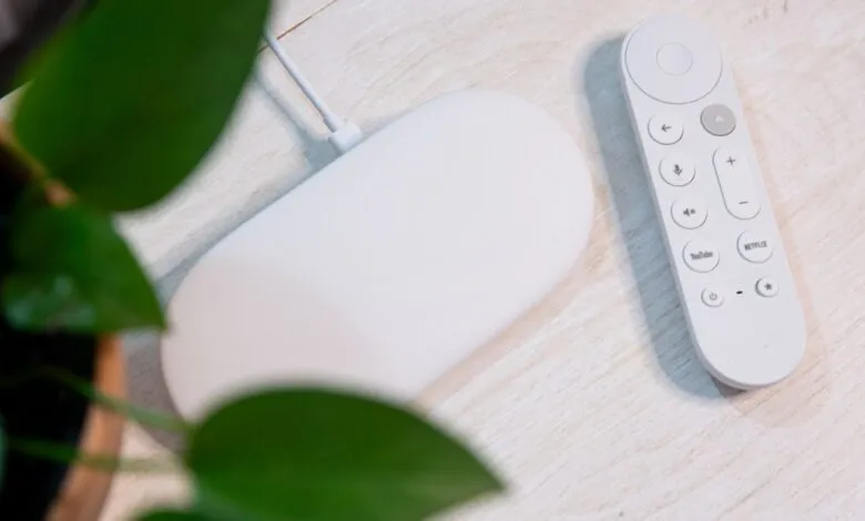 Google Chromecast with Google TV and remote on a light wood surface.
