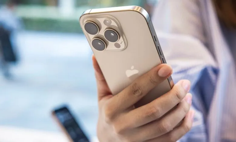Person holds a gold iPhone with three camera lenses in their hand.