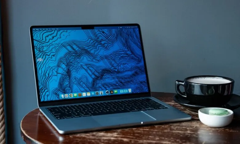MacBook Air on wooden table with coffee and macaron, blue topographic screen.