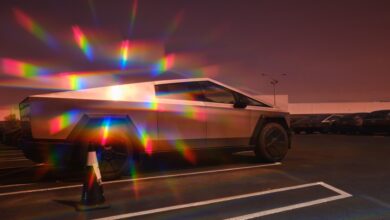 Tesla Cybertruck parked in lot, reflecting rainbow light prisms.
