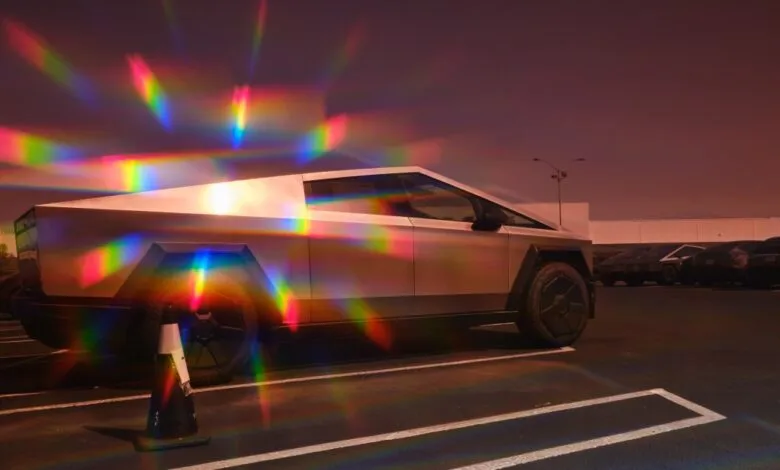 Tesla Cybertruck parked in lot, reflecting rainbow light prisms.