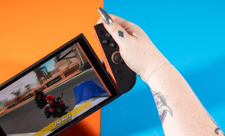 Nintendo Switch OLED being held, Mario Kart game displayed.