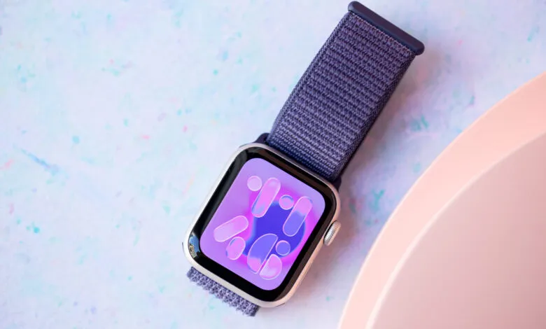 Apple Watch SE with purple band on a colorful speckled surface.