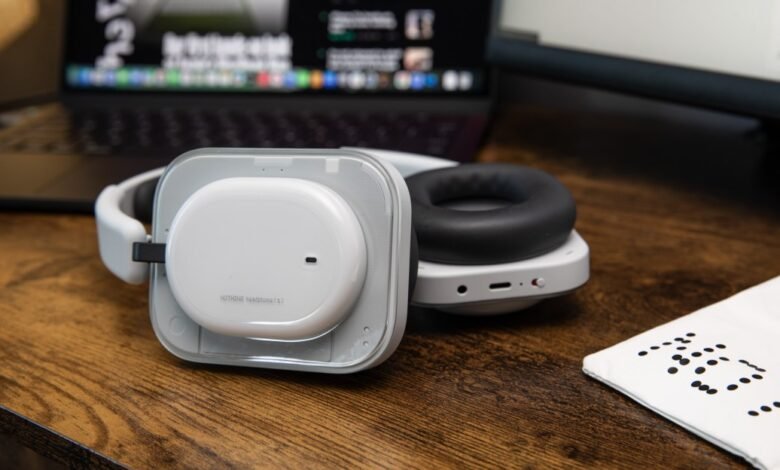 Nothing Headphones (2) on a wooden desk with a laptop and monitor in the background.