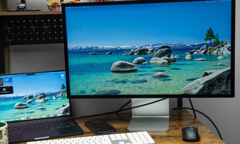 Apple Studio Display and MacBook Pro on a desk showing a scenic lake.