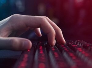 Close-up of a hand typing on a red backlit keyboard in a dark room.