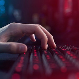 Close-up of a hand typing on a red backlit keyboard in a dark room.