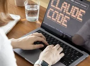 Person types on laptop displaying 'Claude Code' welcome screen, with glass of water nearby.