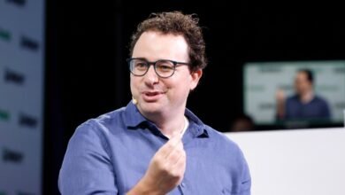 Man with glasses gestures during a presentation on stage.
