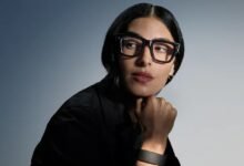 Woman with dark hair wearing large black Ray-Ban glasses, looking thoughtful.