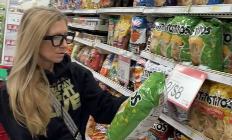 Woman with glasses shops for chips in a grocery store aisle.