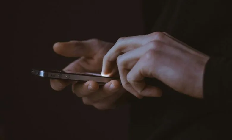 Hands using a smartphone in a dimly lit environment.