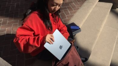 Person putting a blue Apple MacBook Air into a maroon backpack on stone steps.