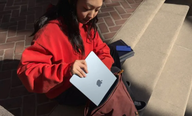 Person putting a blue Apple MacBook Air into a maroon backpack on stone steps.