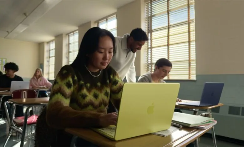 Students use colorful MacBooks in a sunlit classroom setting.
