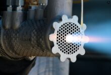 Close-up of metal Arbor device with bright light emanating from a perforated gear-shaped end.