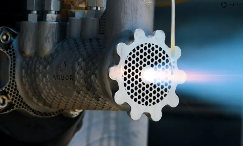 Close-up of metal Arbor device with bright light emanating from a perforated gear-shaped end.