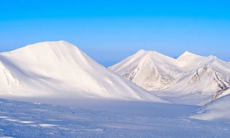 Snow-covered mountains under a clear blue sky, arctic landscape.