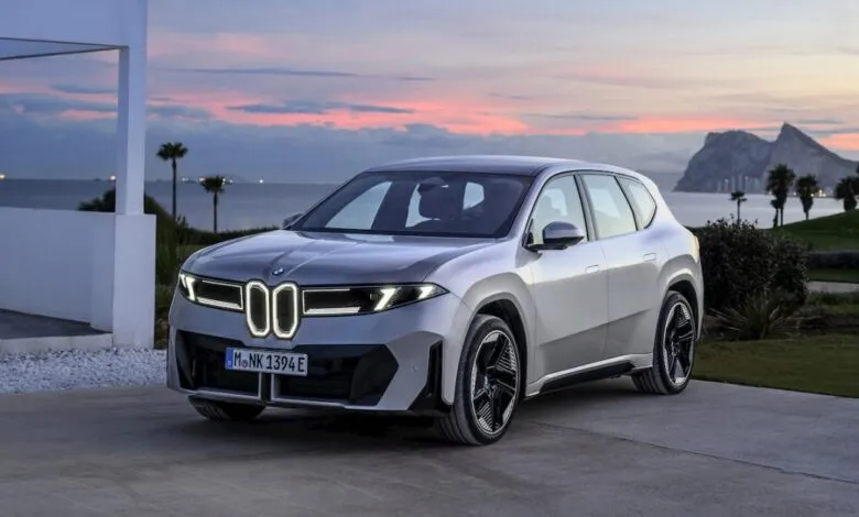 Silver BMW iX3 electric SUV parked with coastal sunset backdrop.
