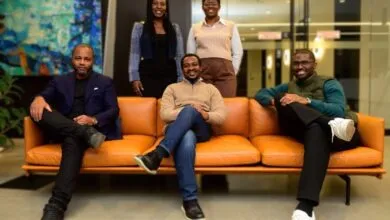 Group of five diverse professionals posing on and behind a modern orange couch.