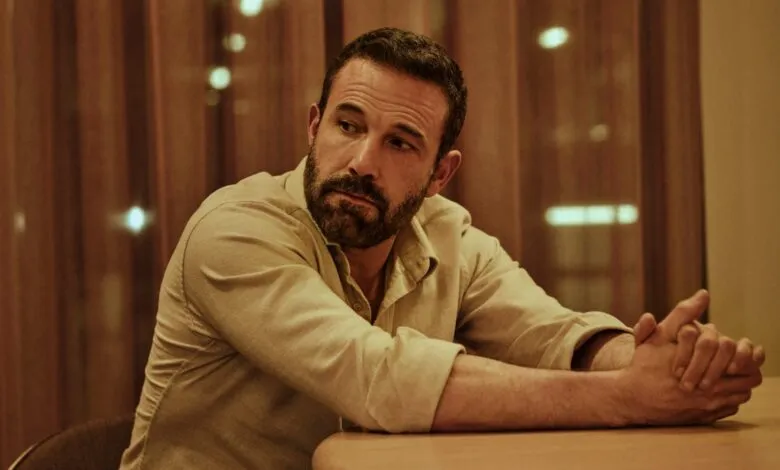 Ben Affleck sits at a table with his hands clasped, looking off to the side.