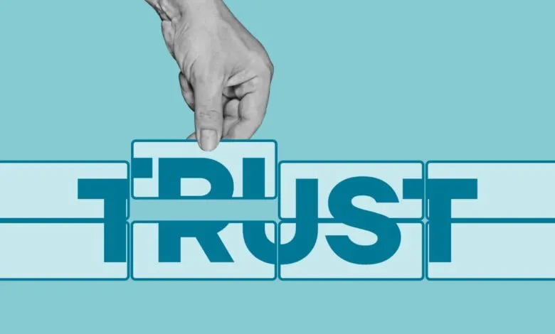 Hand placing block to complete the word TRUST on a blue background.