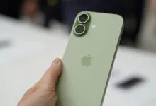 Hand holding a green iPhone with dual camera system and Apple logo.