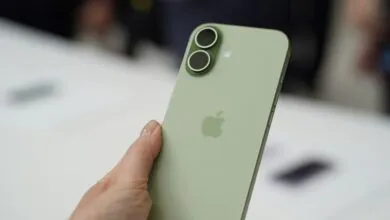 Hand holding a green iPhone with dual camera system and Apple logo.