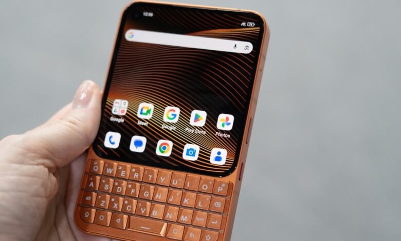 Hand holding a small, bronze-colored smartphone with a physical keyboard.