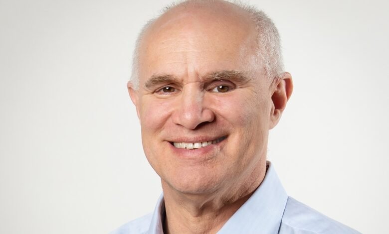 Smiling man with light skin and a blue shirt against a white background.