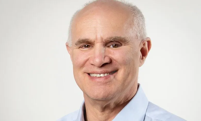Smiling man with light skin and a blue shirt against a white background.