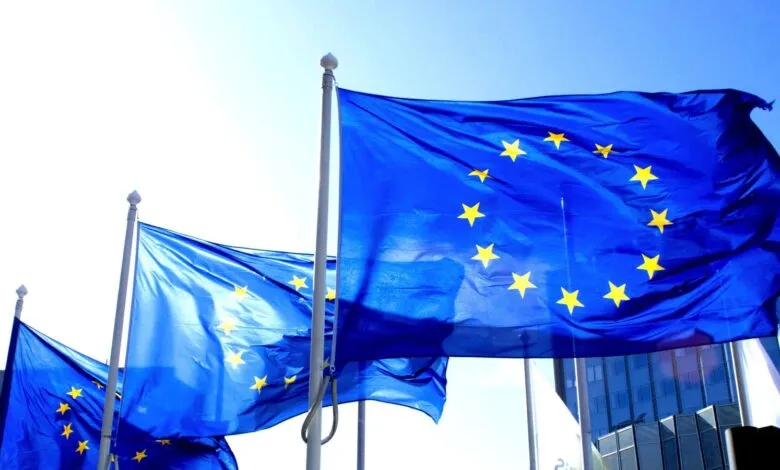 Several European Union flags waving against a bright blue sky.