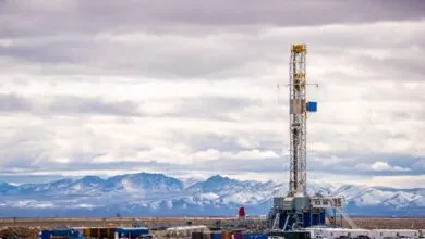Geothermal drilling rig stands tall against a backdrop of snow-capped mountains and cloudy sky.