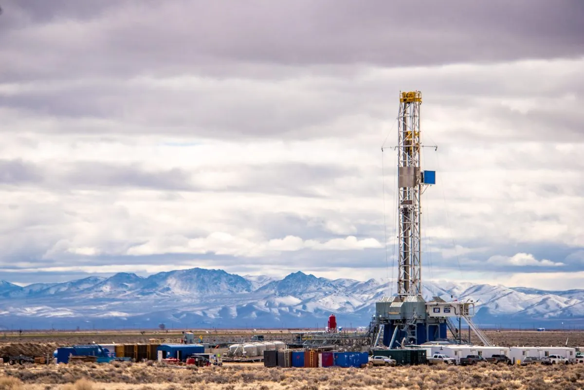 Geothermal drilling rig stands tall against a backdrop of snow-capped mountains and cloudy sky.
