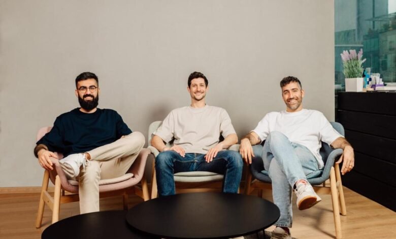 Three men sit in chairs, smiling, in a modern office setting.