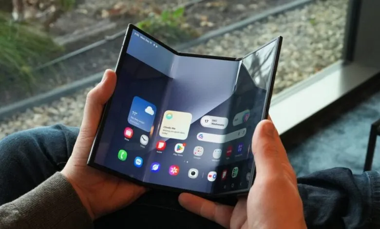 Person holds a tri-fold smartphone displaying a home screen with app icons.