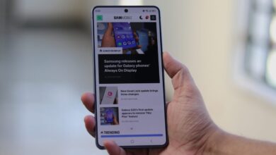 Hand holding smartphone displaying SamMobile website with tech news.