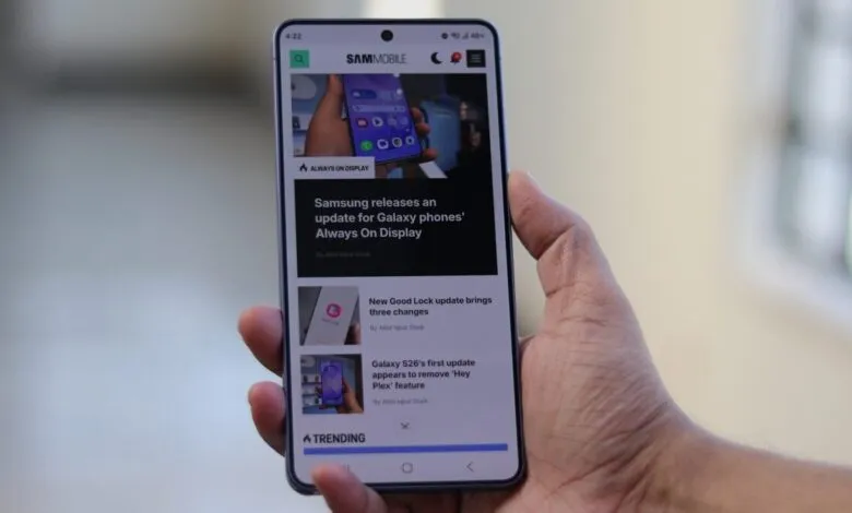 Hand holding smartphone displaying SamMobile website with tech news.
