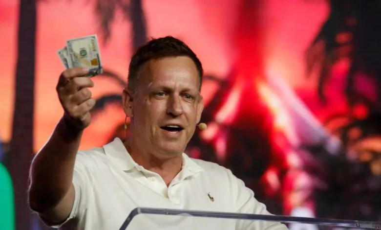 Peter Thiel holds up cash on stage at event.