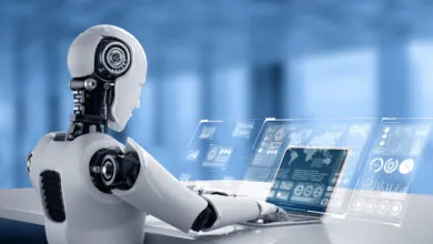 White humanoid robot using laptop with data visualizations on screen.