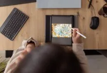 Person drawing digital art on tablet at desk with keyboard and coffee.