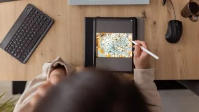 Person drawing digital art on tablet at desk with keyboard and coffee.