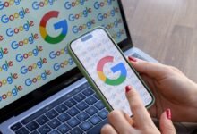 Woman's hand interacts with Google logo on phone screen next to laptop.