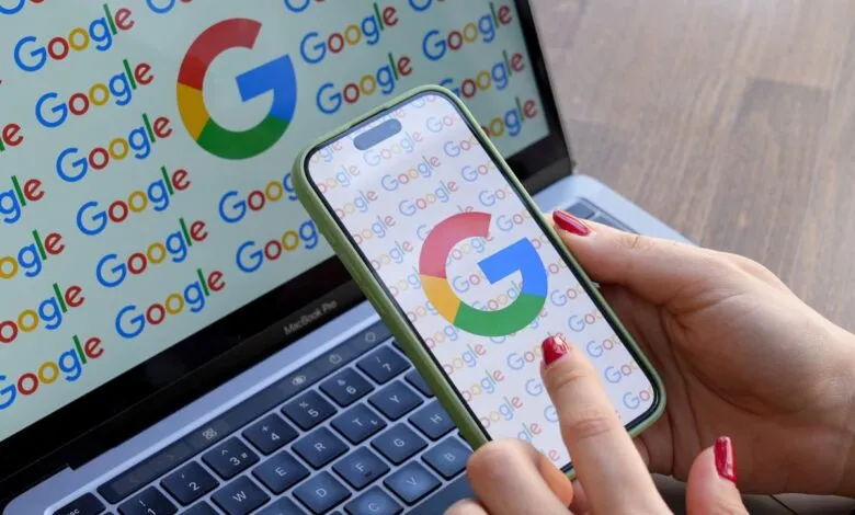 Woman's hand interacts with Google logo on phone screen next to laptop.